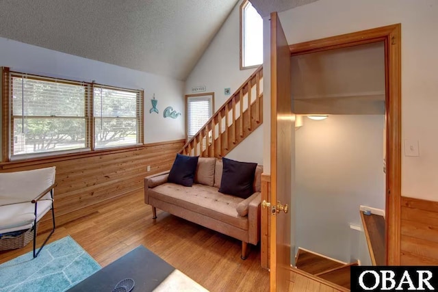 sitting room with a textured ceiling, light wood-style flooring, wood walls, vaulted ceiling, and wainscoting