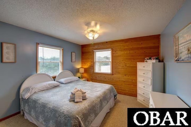 bedroom featuring a textured ceiling, wooden walls, a ceiling fan, and light colored carpet