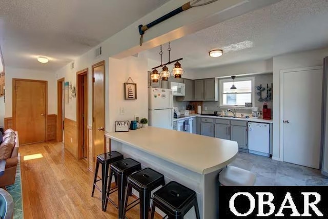 kitchen featuring white appliances, hanging light fixtures, a peninsula, gray cabinets, and light countertops