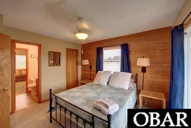 bedroom with a ceiling fan, connected bathroom, light colored carpet, and wooden walls