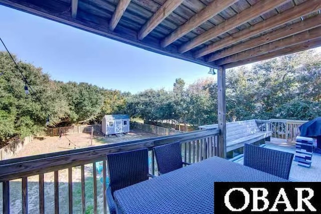 wooden deck with a storage shed, outdoor dining area, an outdoor structure, and a fenced backyard