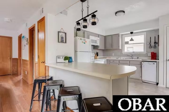 kitchen with gray cabinets, light countertops, white appliances, a peninsula, and a kitchen bar