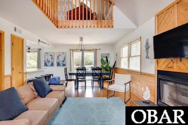 living area featuring visible vents, a glass covered fireplace, wainscoting, wooden walls, and wood finished floors