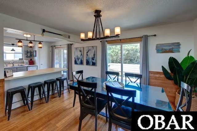 dining space with a textured ceiling, light wood finished floors, and a notable chandelier