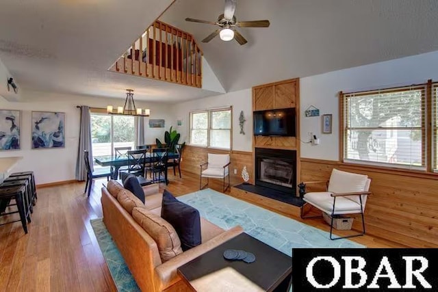 living room featuring high vaulted ceiling, light wood-type flooring, a fireplace, and ceiling fan with notable chandelier