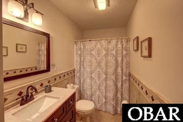 bathroom featuring tile walls, toilet, wainscoting, vanity, and a textured ceiling