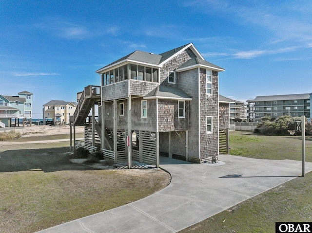 view of front of property featuring stairs, concrete driveway, a front lawn, and a sunroom