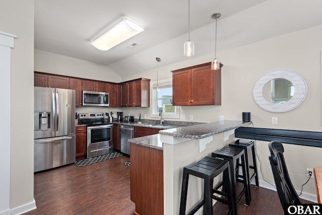 kitchen with stainless steel appliances, a peninsula, a sink, dark stone counters, and pendant lighting