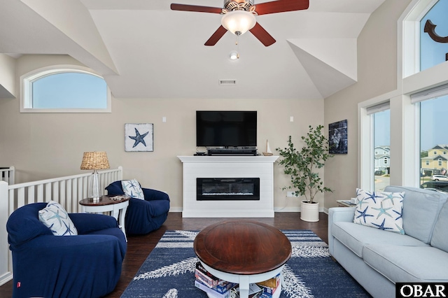 living area featuring visible vents, vaulted ceiling, dark wood-style flooring, and a glass covered fireplace