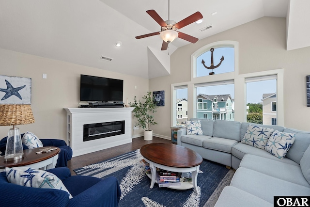 living room with dark wood-style floors, visible vents, a ceiling fan, and a glass covered fireplace