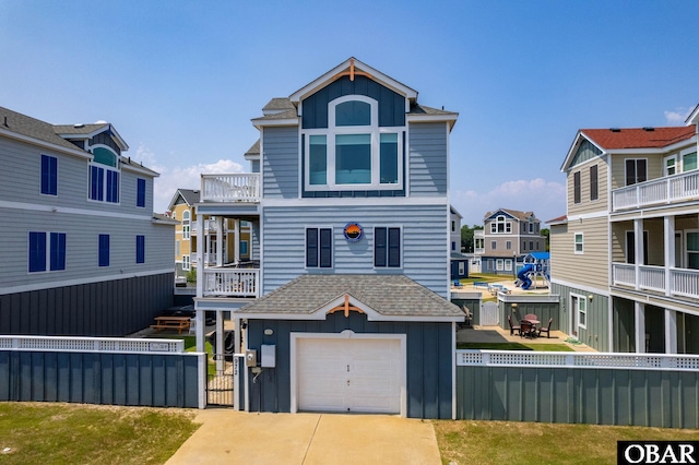 coastal inspired home with concrete driveway, an attached garage, a balcony, fence private yard, and a residential view