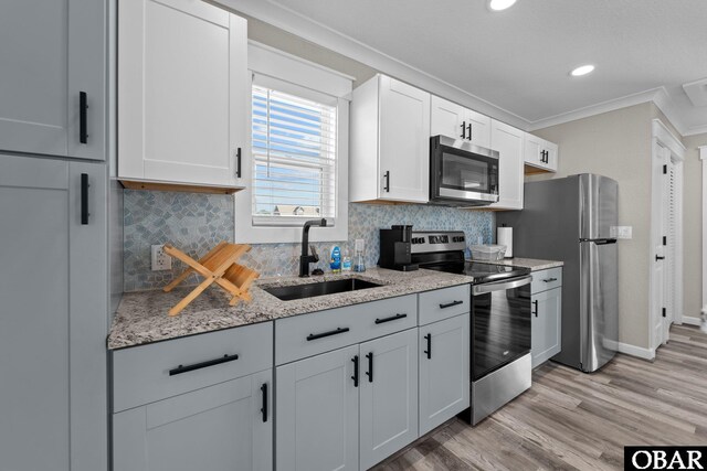 kitchen featuring crown molding, appliances with stainless steel finishes, light wood-style floors, white cabinetry, and a sink