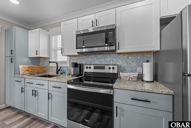 kitchen with tasteful backsplash, white cabinets, appliances with stainless steel finishes, light stone countertops, and a sink