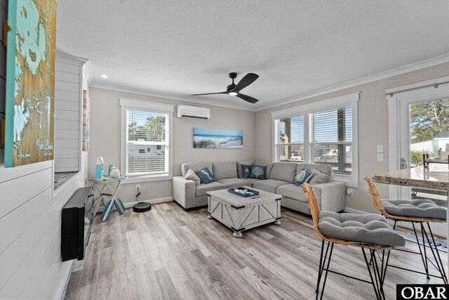 living room featuring light wood finished floors, baseboards, ceiling fan, ornamental molding, and a wall mounted air conditioner