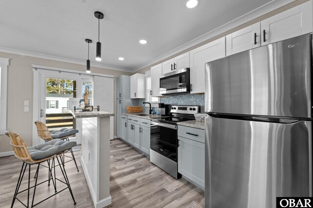 kitchen featuring light stone counters, decorative light fixtures, appliances with stainless steel finishes, white cabinets, and a kitchen breakfast bar