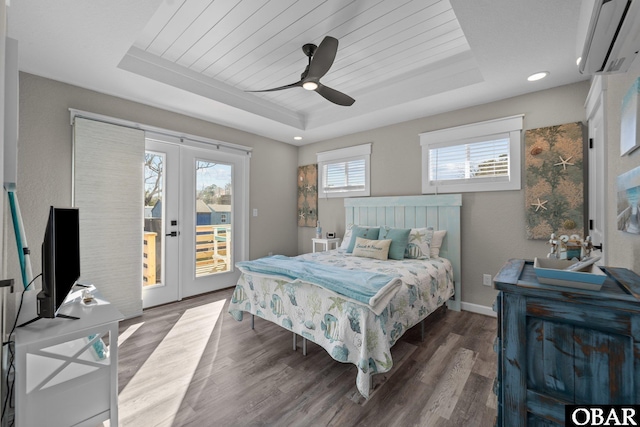 bedroom featuring a wall unit AC, wood finished floors, access to exterior, a tray ceiling, and french doors