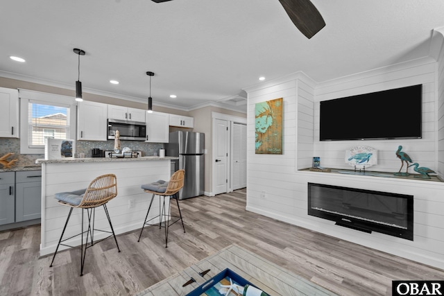 kitchen with decorative light fixtures, a breakfast bar area, stainless steel appliances, a large fireplace, and white cabinets