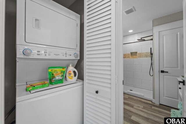 washroom featuring stacked washing maching and dryer, laundry area, visible vents, and wood finished floors