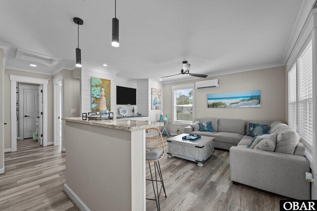 living area featuring baseboards, a wall unit AC, light wood-style flooring, and crown molding