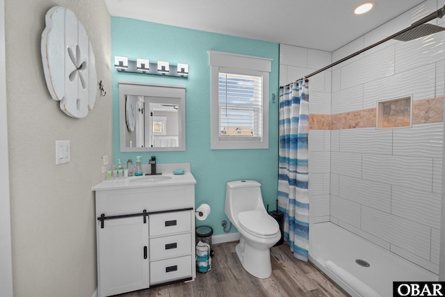 bathroom featuring toilet, a stall shower, vanity, wood finished floors, and baseboards