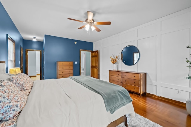 bedroom with ceiling fan, wood finished floors, and a decorative wall