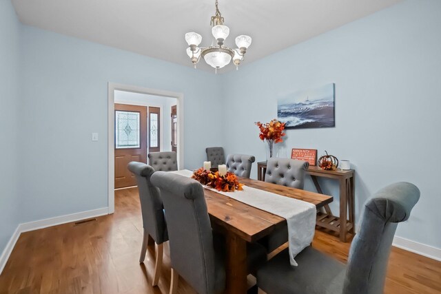 dining space featuring a notable chandelier, wood finished floors, visible vents, and baseboards