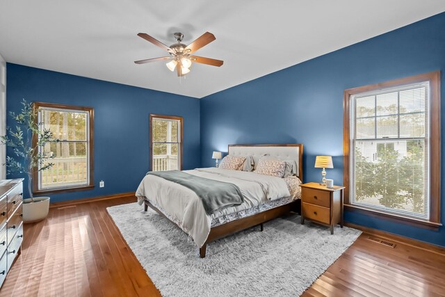 bedroom with ceiling fan, visible vents, multiple windows, and wood-type flooring