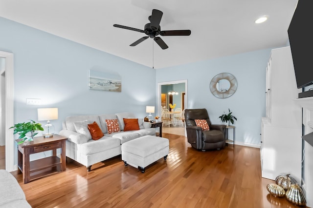 living area with wood finished floors, a fireplace, and ceiling fan with notable chandelier