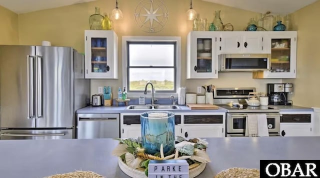 kitchen with appliances with stainless steel finishes, white cabinetry, glass insert cabinets, and hanging light fixtures