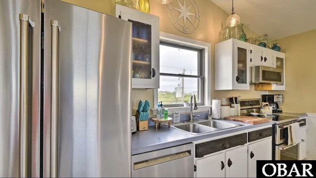 kitchen with pendant lighting, stainless steel appliances, a sink, and white cabinets