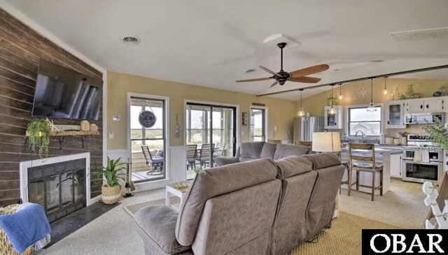 living room with a wainscoted wall, a large fireplace, a healthy amount of sunlight, and light carpet