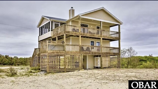 view of front of home with a deck, a sunroom, a chimney, and stairs