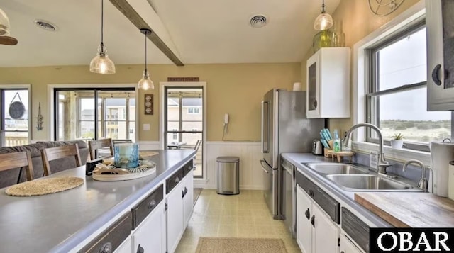 kitchen with a wainscoted wall, decorative light fixtures, visible vents, white cabinets, and a sink