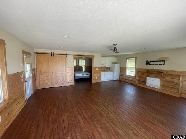 102 Daybreak Ct Lot # 53, Grandy, NC 27939 - unfurnished living room with a ceiling fan, dark wood-style floors, a barn door, a wainscoted wall, and a textured ceiling