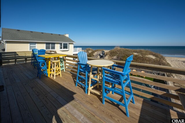 deck with outdoor dining space, a water view, and a beach view