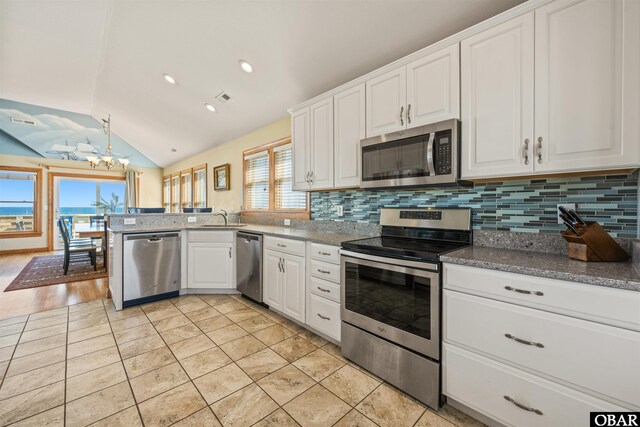 kitchen featuring tasteful backsplash, lofted ceiling, appliances with stainless steel finishes, a peninsula, and white cabinetry