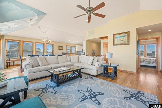 living area featuring visible vents, light wood-style flooring, vaulted ceiling, baseboards, and ceiling fan with notable chandelier