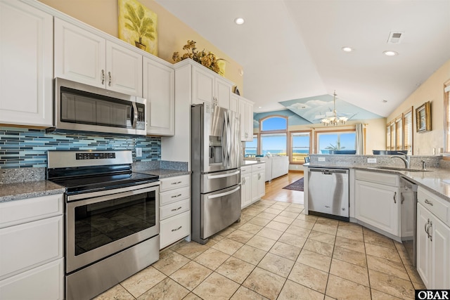 kitchen with light stone countertops, vaulted ceiling, appliances with stainless steel finishes, and white cabinets