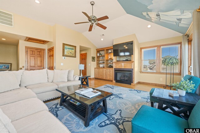 living area with light wood finished floors, recessed lighting, visible vents, a glass covered fireplace, and vaulted ceiling