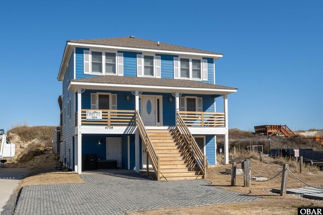 raised beach house featuring a carport, a porch, roof with shingles, and driveway