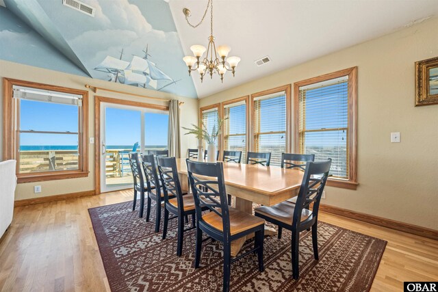 dining space with a water view, light wood-style floors, visible vents, and a notable chandelier