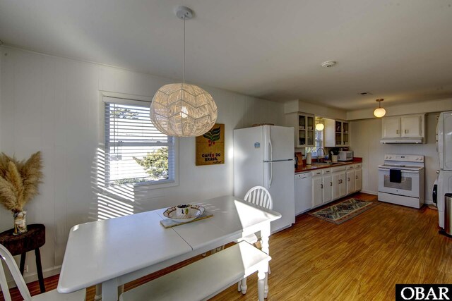 kitchen with under cabinet range hood, white appliances, a sink, hanging light fixtures, and glass insert cabinets