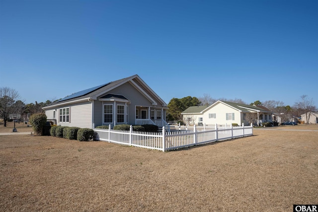 view of front of home featuring a residential view, fence, a front lawn, and solar panels