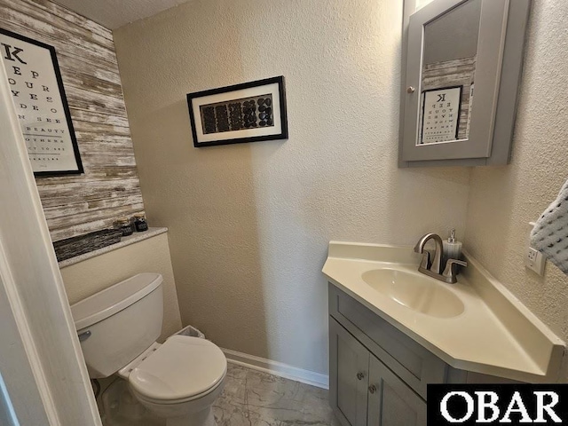 bathroom featuring baseboards, a textured wall, toilet, marble finish floor, and vanity