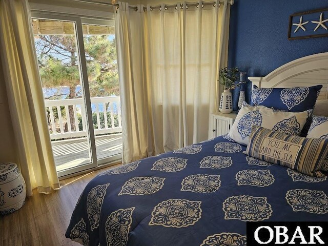 bedroom featuring access to exterior, a textured wall, and wood finished floors