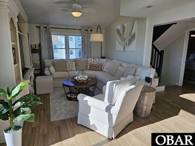 living area featuring lofted ceiling, visible vents, stairway, a ceiling fan, and wood finished floors