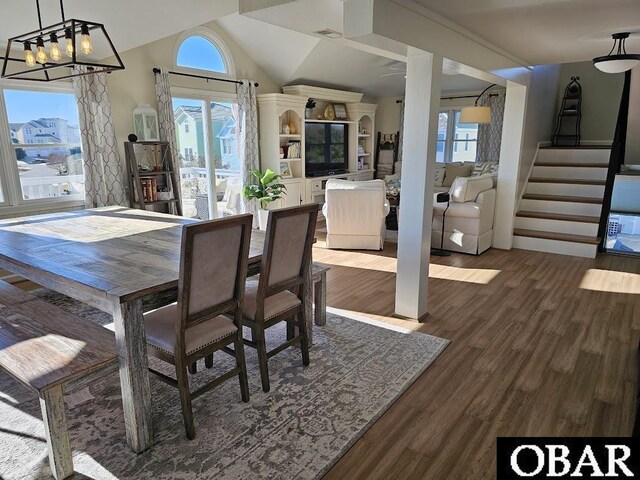 dining area featuring a notable chandelier, wood finished floors, visible vents, stairs, and vaulted ceiling