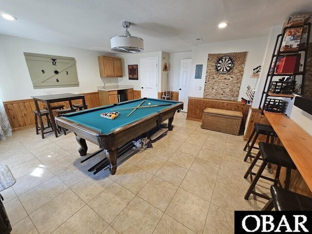 recreation room featuring pool table, wainscoting, light tile patterned flooring, wooden walls, and a textured ceiling