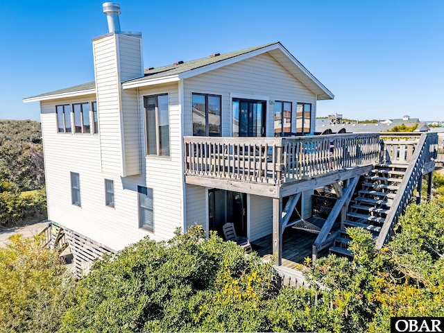 back of property with a chimney, a wooden deck, and stairs