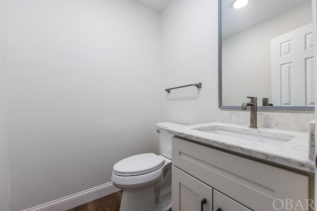 half bath featuring toilet, wood finished floors, vanity, and baseboards